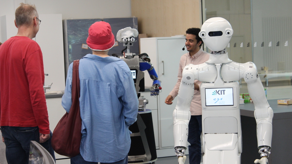 Der humanoide Roboter ARMAR-7 steht neben Besuchern des H2T und einem Mitarbeiter des Lehrstuhls