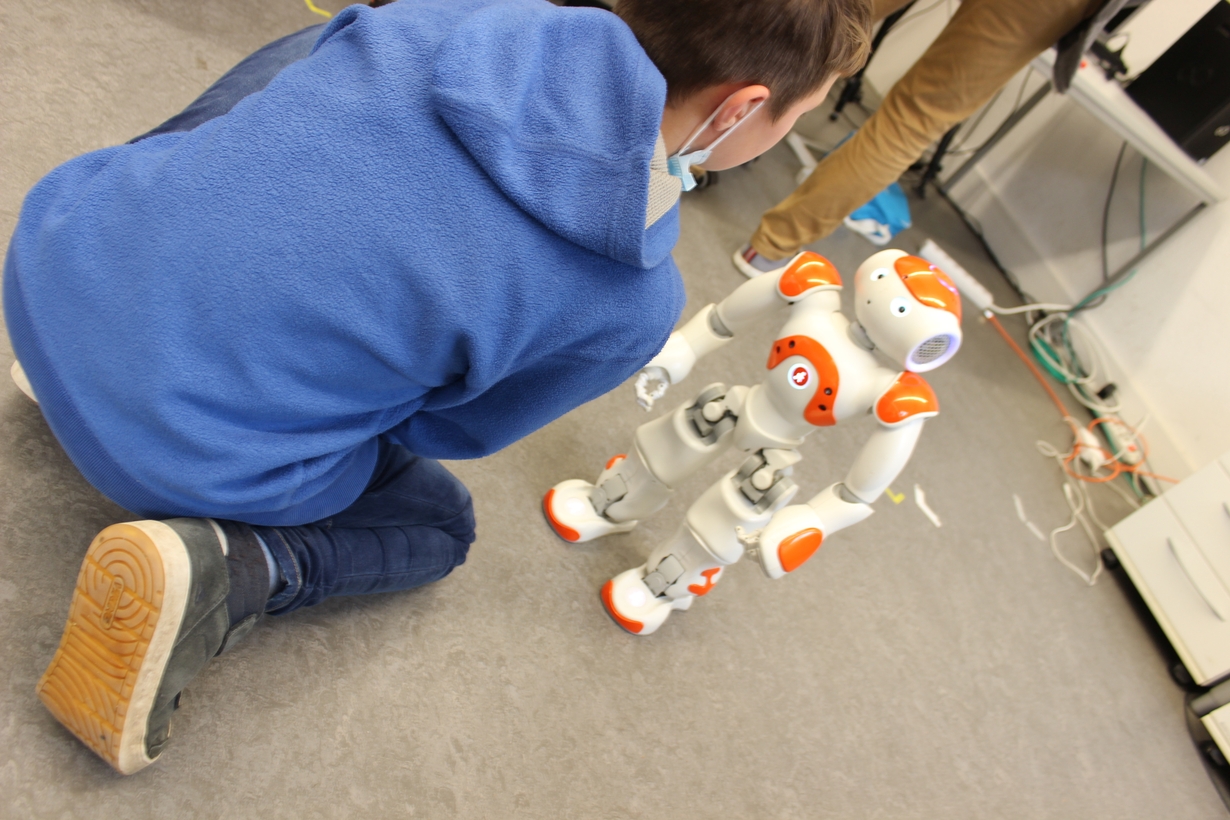 Ein Junge kniet vor dem humanoiden Roboter NAO um mit ihm zu interagieren